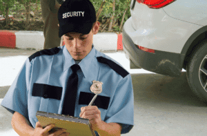 Security officer writing a report on a clipboard near a parked vehicle.